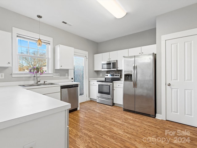 kitchen featuring appliances with stainless steel finishes, sink, light hardwood / wood-style floors, white cabinetry, and hanging light fixtures