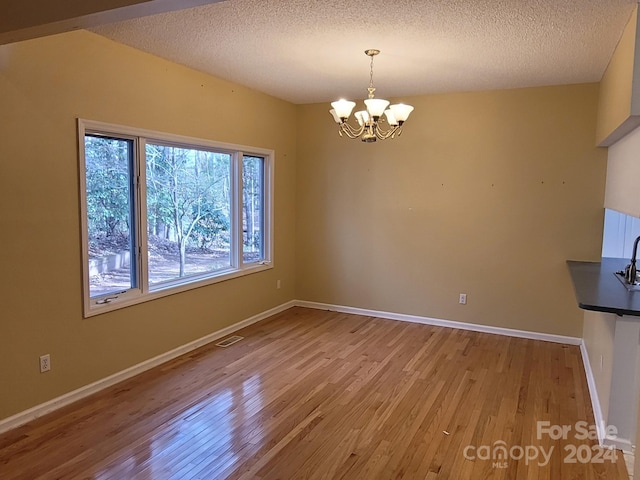 unfurnished dining area with a chandelier, a textured ceiling, and light hardwood / wood-style flooring