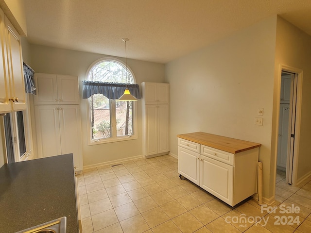 kitchen with wood counters, white cabinets, hanging light fixtures, and light tile patterned flooring