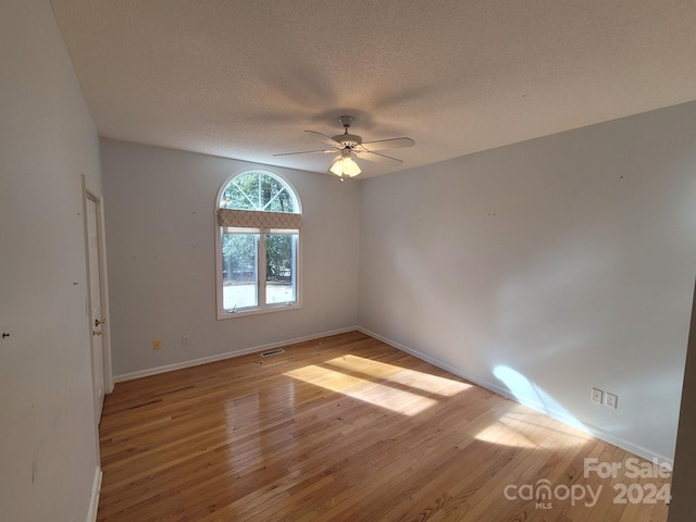 empty room with a textured ceiling, light wood-type flooring, and ceiling fan