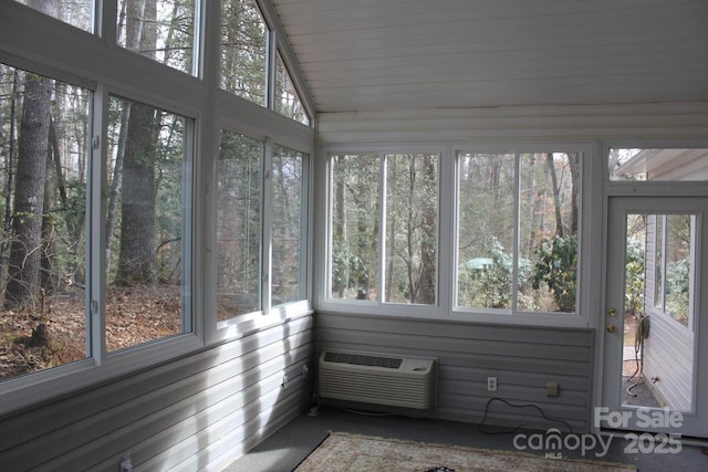 unfurnished sunroom with lofted ceiling, a healthy amount of sunlight, and a wall mounted air conditioner