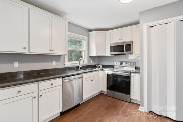 kitchen featuring appliances with stainless steel finishes, dark hardwood / wood-style flooring, sink, dark stone countertops, and white cabinetry