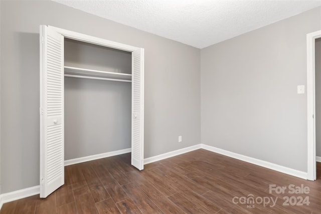 unfurnished bedroom with a textured ceiling, dark wood-type flooring, and a closet