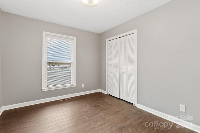 unfurnished bedroom with dark hardwood / wood-style floors, a textured ceiling, and a closet