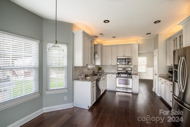 kitchen featuring appliances with stainless steel finishes, dark wood-type flooring, sink, pendant lighting, and white cabinetry