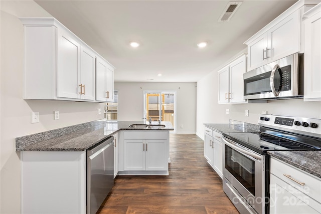 kitchen with sink, appliances with stainless steel finishes, white cabinetry, dark hardwood / wood-style flooring, and kitchen peninsula