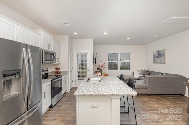 kitchen featuring white cabinets, appliances with stainless steel finishes, a kitchen bar, an island with sink, and sink