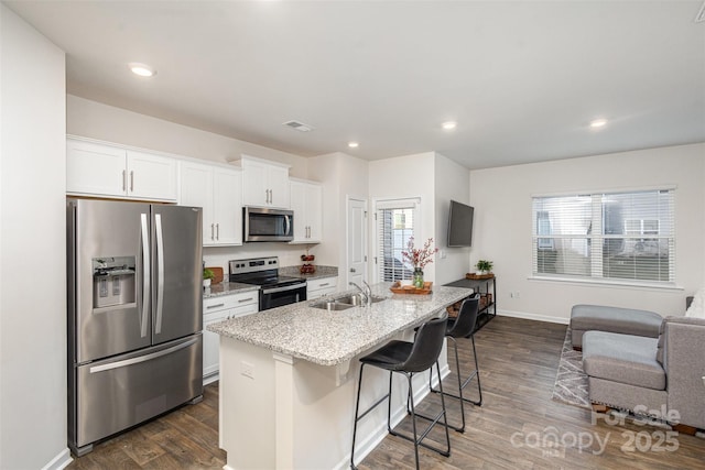 kitchen with white cabinetry, stainless steel appliances, an island with sink, sink, and a breakfast bar