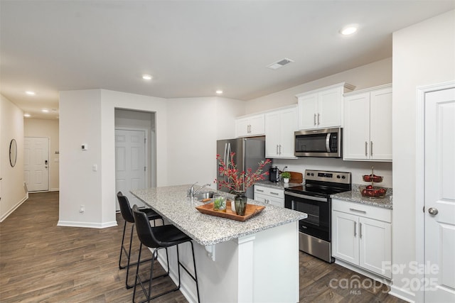 kitchen with white cabinets, an island with sink, light stone counters, and appliances with stainless steel finishes