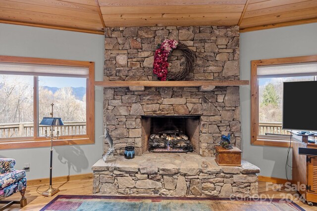 living room featuring a stone fireplace, wooden ceiling, and light wood-type flooring