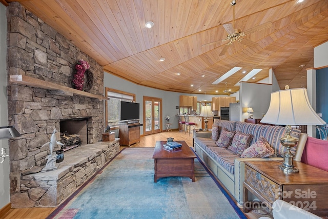 living room featuring a skylight, ceiling fan, a stone fireplace, light hardwood / wood-style flooring, and wood ceiling