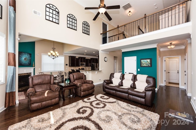 living room featuring a high ceiling, a premium fireplace, dark hardwood / wood-style floors, ceiling fan with notable chandelier, and ornamental molding