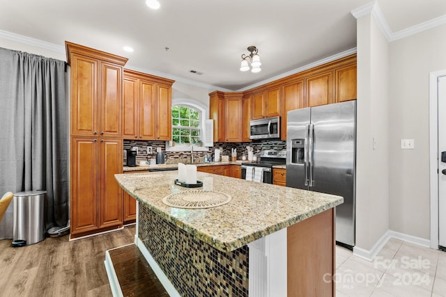 kitchen with a kitchen island, light stone counters, ornamental molding, and appliances with stainless steel finishes