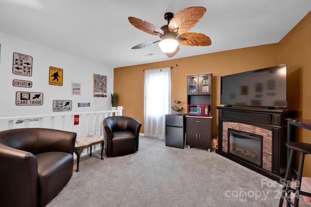 living room featuring light colored carpet, a stone fireplace, and ceiling fan