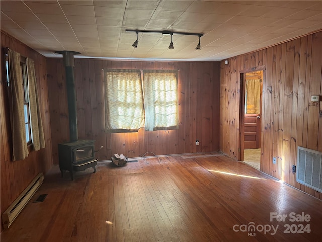 spare room with hardwood / wood-style floors, a baseboard radiator, a wood stove, and wood walls