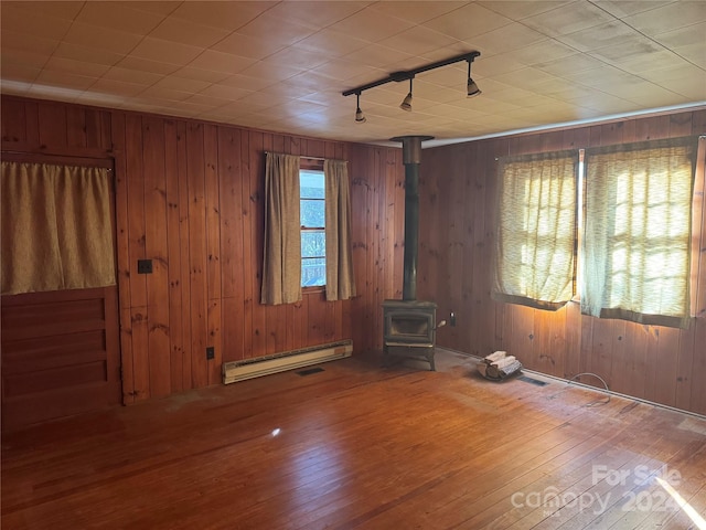 interior space with track lighting, wooden walls, a baseboard heating unit, hardwood / wood-style flooring, and a wood stove