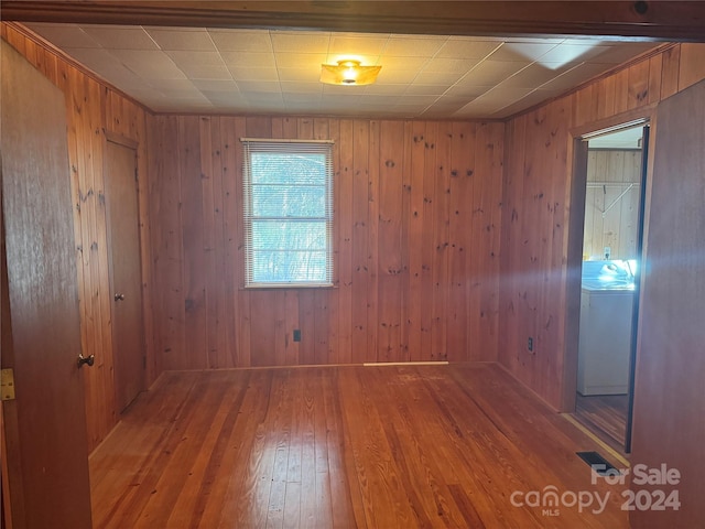 unfurnished room with hardwood / wood-style flooring, washer / clothes dryer, and wooden walls