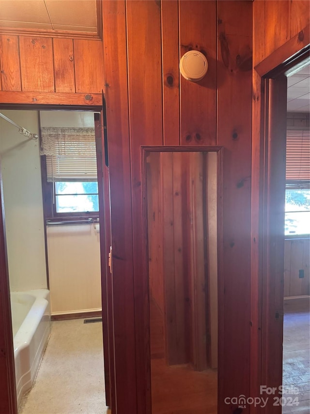 bathroom featuring a wealth of natural light, a tub to relax in, and wooden walls