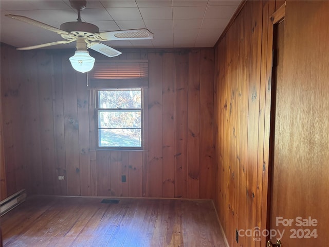 unfurnished room featuring hardwood / wood-style flooring, a baseboard radiator, and wooden walls