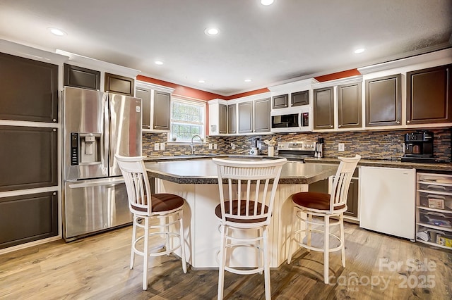 kitchen featuring a kitchen island, appliances with stainless steel finishes, sink, a kitchen breakfast bar, and light wood-type flooring