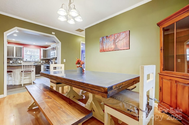 dining area with ornamental molding, an inviting chandelier, and light hardwood / wood-style floors