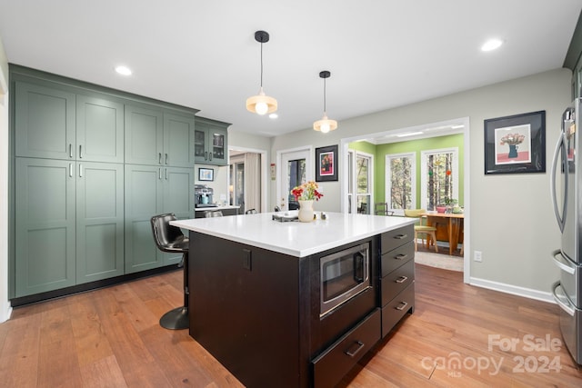 kitchen with a center island, light hardwood / wood-style flooring, decorative light fixtures, appliances with stainless steel finishes, and green cabinetry