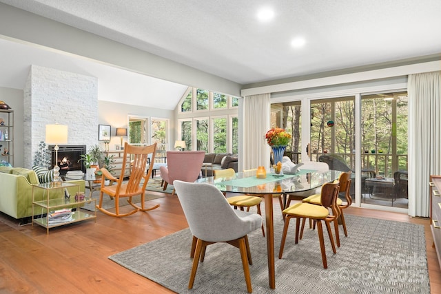 dining area with lofted ceiling, a healthy amount of sunlight, a stone fireplace, and hardwood / wood-style floors