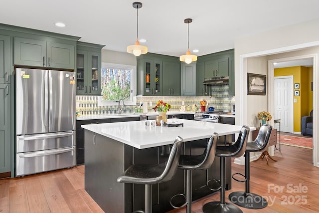 kitchen with a kitchen island, appliances with stainless steel finishes, pendant lighting, decorative backsplash, and light hardwood / wood-style flooring