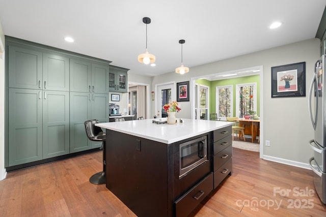 kitchen with appliances with stainless steel finishes, pendant lighting, a center island, green cabinets, and light hardwood / wood-style floors