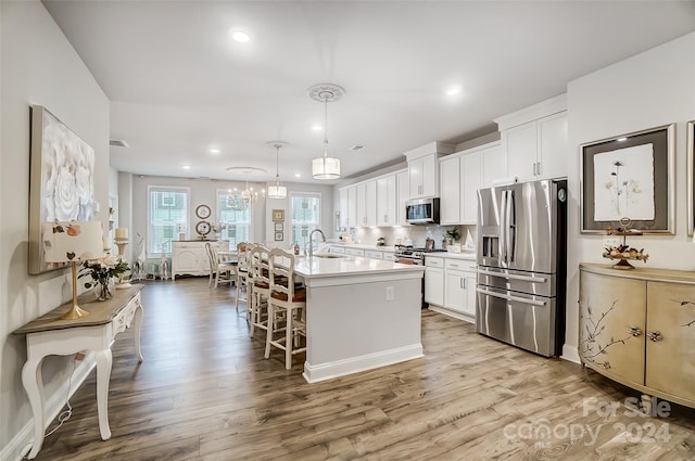 kitchen with white cabinetry, pendant lighting, stainless steel appliances, and light hardwood / wood-style floors