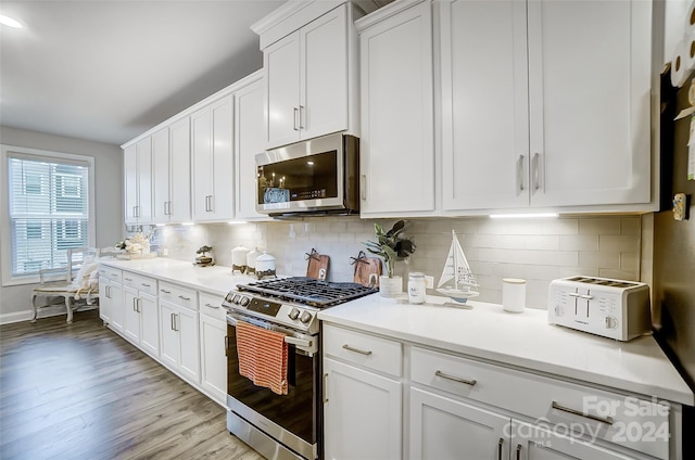 kitchen with white cabinets, light hardwood / wood-style floors, backsplash, and appliances with stainless steel finishes