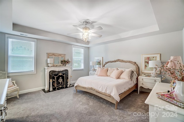 bedroom featuring dark carpet, a raised ceiling, multiple windows, and ceiling fan