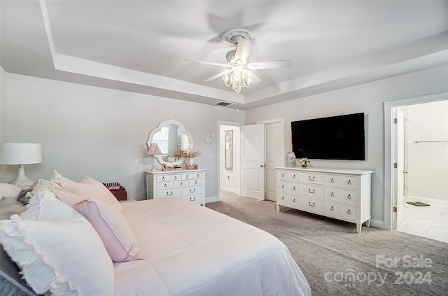 carpeted bedroom featuring a tray ceiling, connected bathroom, and ceiling fan