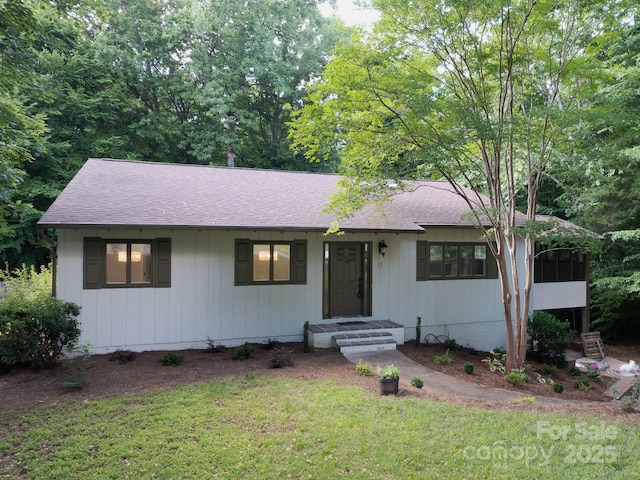 ranch-style house with a sunroom, roof with shingles, and a front lawn