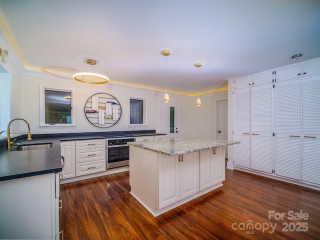 kitchen featuring oven, dark wood-type flooring, a sink, white cabinets, and decorative light fixtures