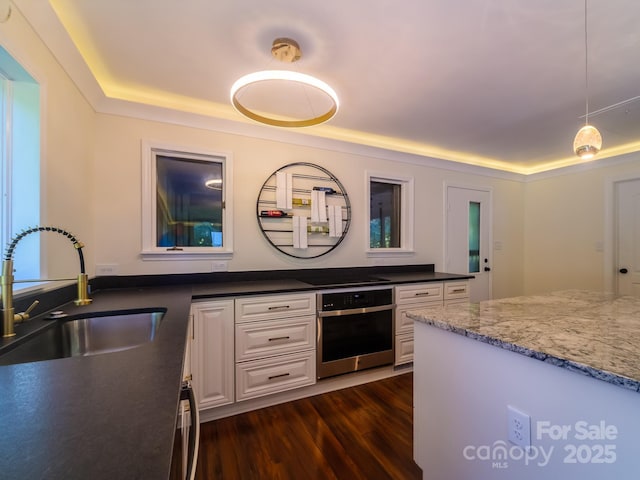 kitchen featuring white cabinets, a tray ceiling, stainless steel oven, pendant lighting, and a sink