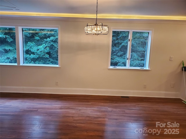 unfurnished dining area with dark wood-style flooring, baseboards, and an inviting chandelier