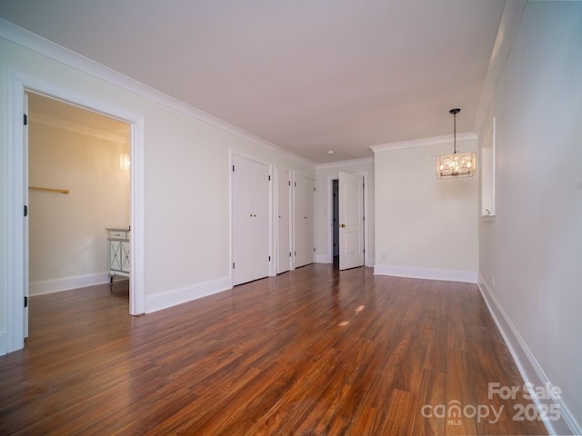 spare room with baseboards, dark wood-type flooring, crown molding, and an inviting chandelier