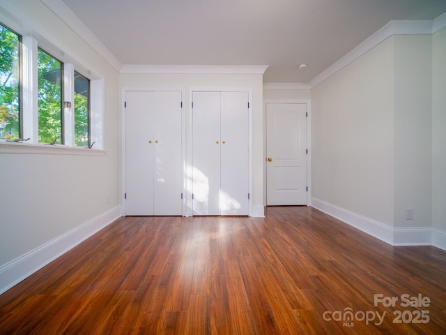 unfurnished bedroom with ornamental molding, multiple closets, dark wood finished floors, and baseboards