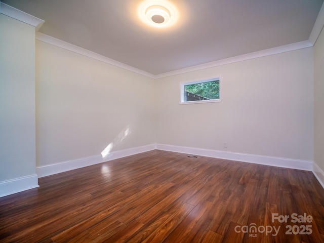 empty room featuring ornamental molding, dark wood-style flooring, visible vents, and baseboards