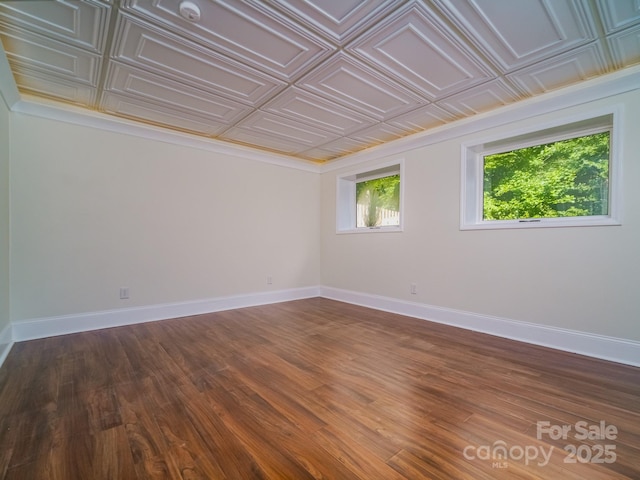 spare room featuring wood finished floors, an ornate ceiling, and baseboards