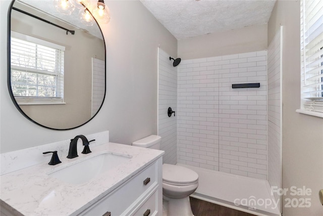 bathroom featuring vanity, toilet, a textured ceiling, and tiled shower