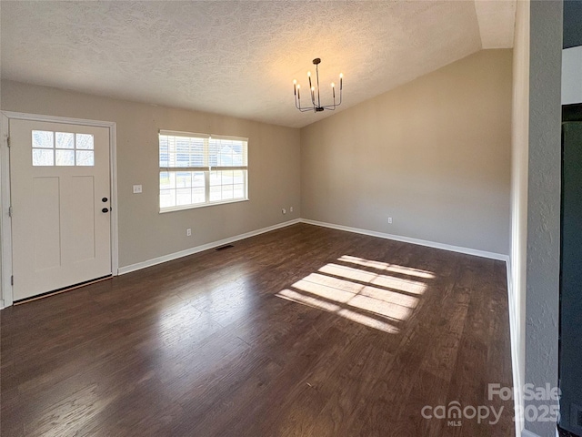 entrance foyer with a textured ceiling, a notable chandelier, wood finished floors, visible vents, and vaulted ceiling