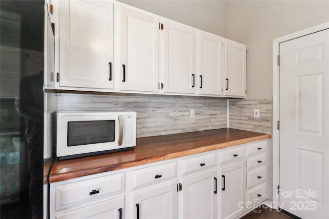 kitchen with wooden counters, white microwave, white cabinetry, and decorative backsplash