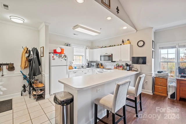 kitchen featuring a breakfast bar, white cabinetry, white appliances, and a wealth of natural light