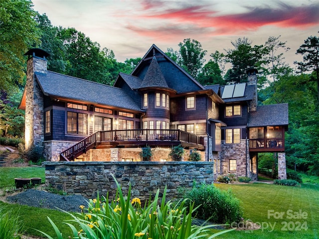 back house at dusk featuring solar panels, a yard, and a wooden deck