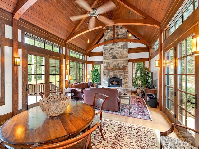 dining room featuring a stone fireplace, light wood-type flooring, french doors, high vaulted ceiling, and beamed ceiling