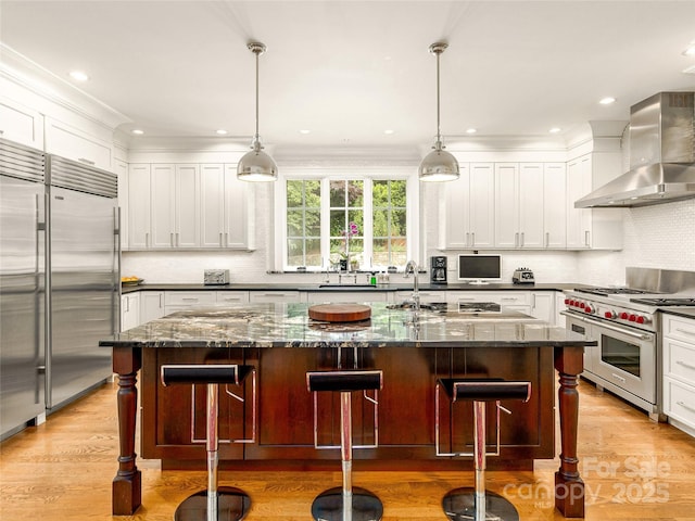 kitchen with a kitchen bar, wall chimney exhaust hood, a kitchen island with sink, and high end appliances