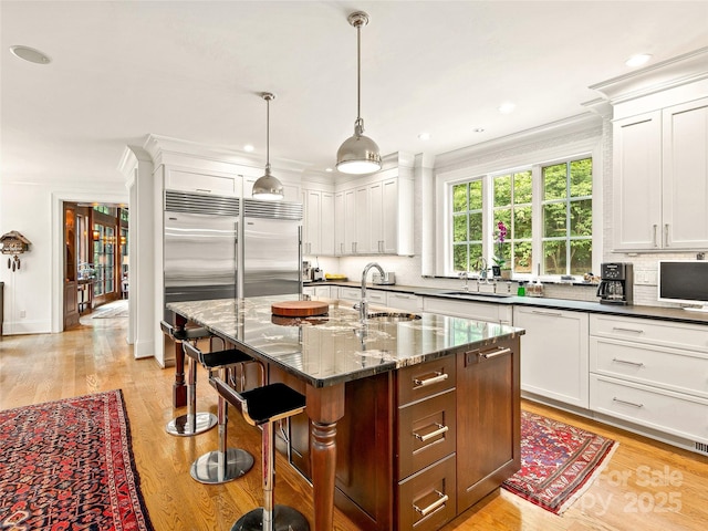 kitchen with dark stone countertops, pendant lighting, sink, paneled dishwasher, and a kitchen island with sink