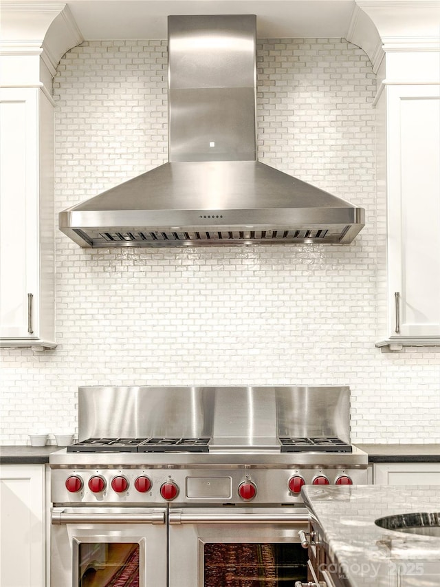 kitchen featuring white cabinets, backsplash, double oven range, and wall chimney exhaust hood